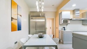 Una cucina moderna con elettrodomestici in acciaio inox, un tavolo da pranzo bianco con sedie e una lampada a sospensione.