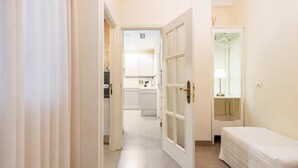 Un corridoio stretto conduce a una camera da letto con un letto e un comodino. Una porta si apre su una zona cucina con pensili e un piano di lavoro.
