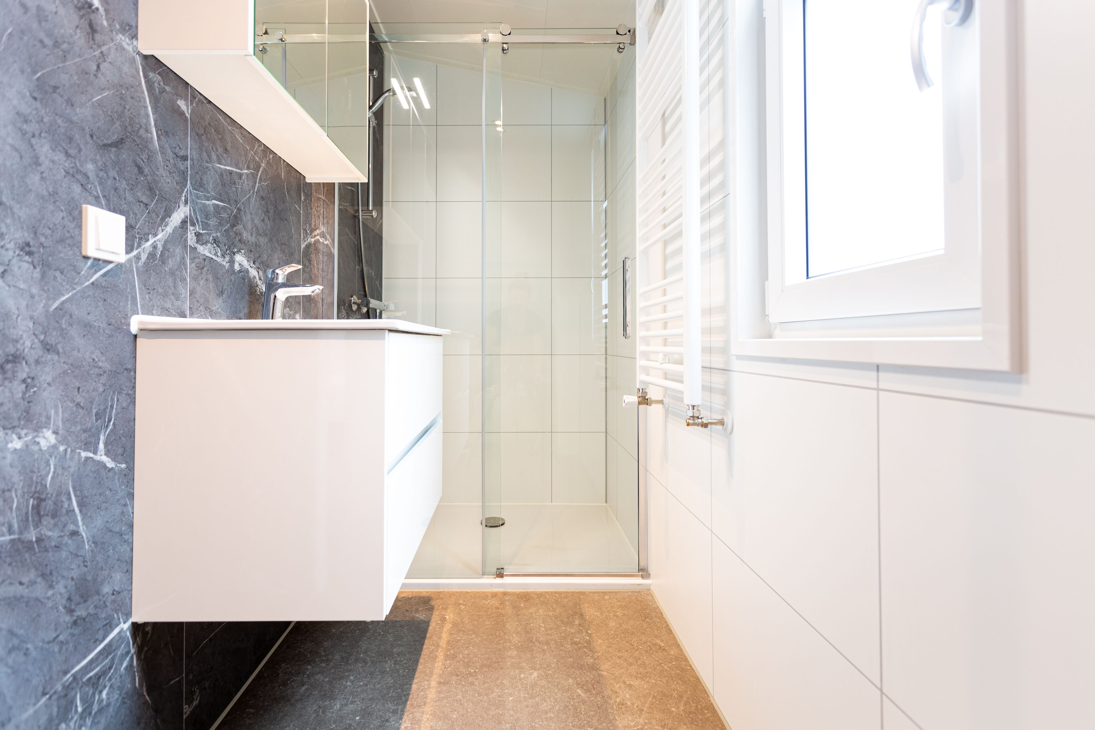 A modern bathroom with a glass shower enclosure, a white vanity, and a marble backsplash.