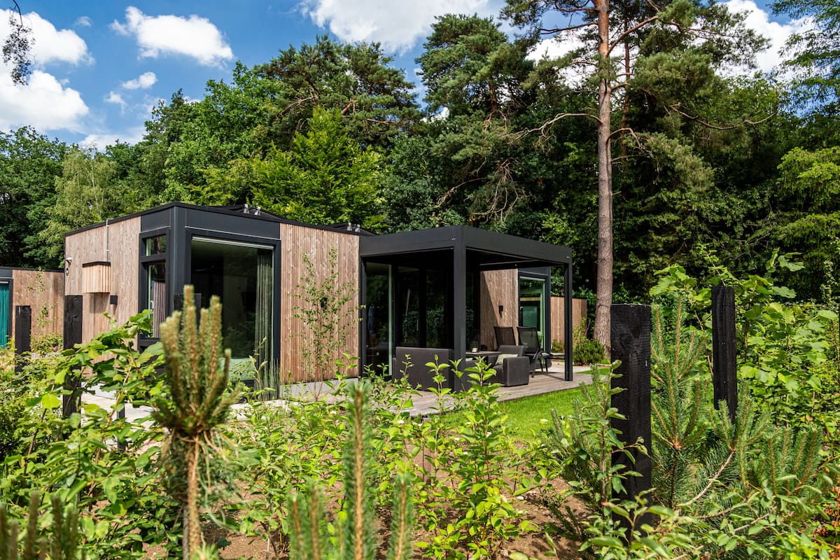 Ett modernt hus med en glasfasad, träpanel på utsidan och en uteplats med utemöbler.