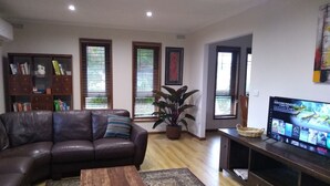 Una sala de estar con un sofá de cuero, una mesa de centro con libros, un televisor sobre un mueble bajo, una estantería y una planta en maceta.