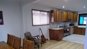 Una cocina amplia con armarios de madera, una zona de comedor con una mesa y sillas de madera, y una guitarra apoyada contra la pared.