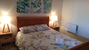Una cama bien hecha con ropa de cama floral, dos lámparas de noche e una pared con tres láminas botánicas enmarcadas.