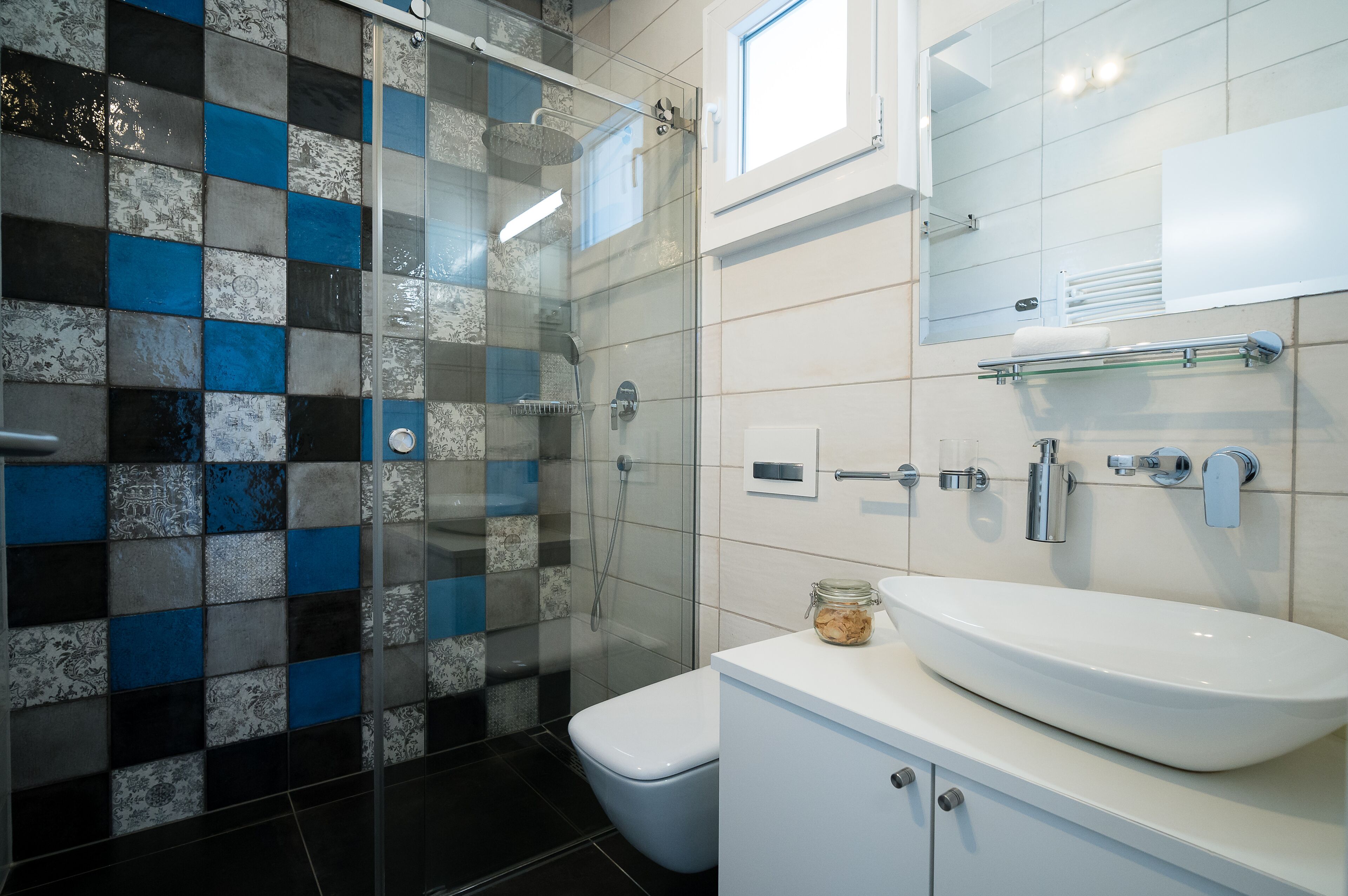 A modern bathroom with a glass shower enclosure, a white sink, and a tiled backsplash.