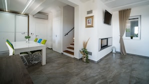 Una sala de estar moderna con comedor, escalera, chimenea y televisor montado en la pared.