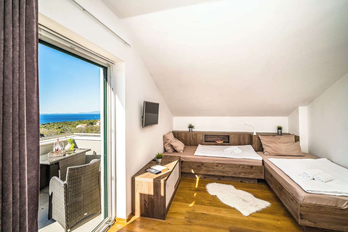 Ein kleines, modernes Schlafzimmer mit Holzboden, einem großen Fenster mit Meerblick, einem integrierten Fernseher und einer gemütlichen Sitzecke.