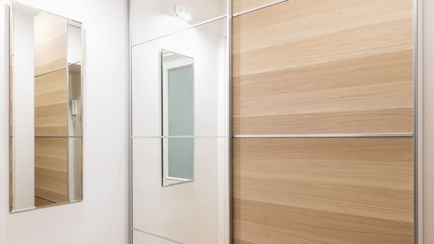 Een moderne kamer met een houten visgraatvloer, een schuifdeur van hout en een grote spiegel aan de wand.