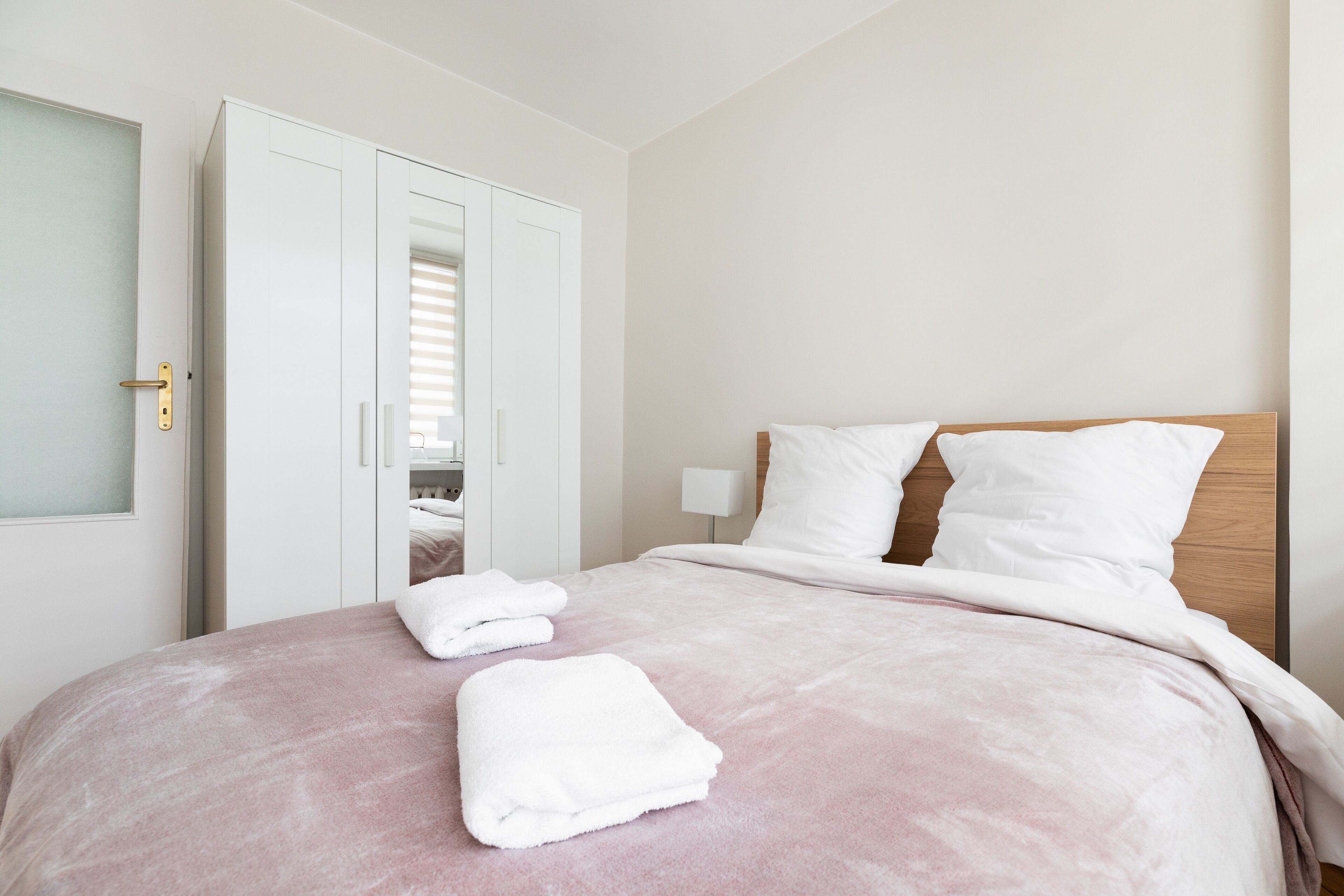 A neatly made bed with white linens and two folded white towels on the bed.