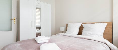 A neatly made bed with white linens and two folded white towels on the bed.