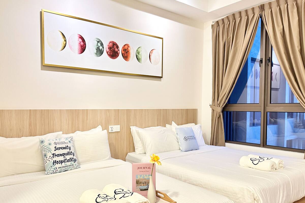 Une chambre d’hôtel avec deux lits, une œuvre d’art encadrée représentant des lunes, une fenêtre avec des rideaux et un journal posé sur le lit de gauche.