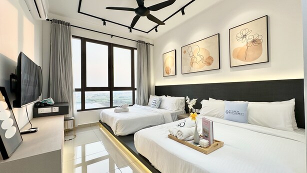 Una habitación de hotel con dos camas, televisión, ventilador de techo, ventanas grandes y obras de arte en las paredes.