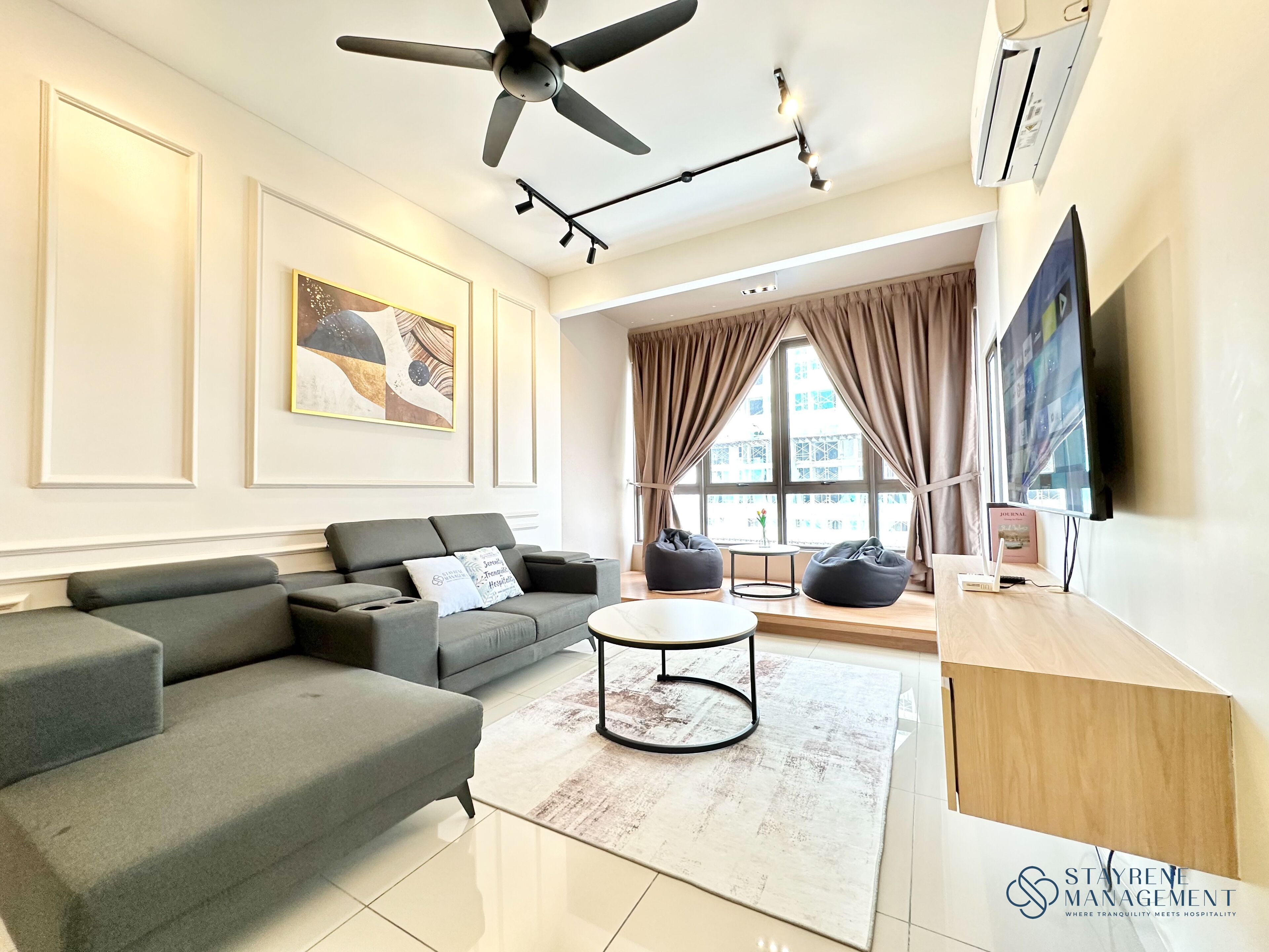A modern living room with a grey sofa, a round coffee table, and a flat-screen TV mounted on the wall.