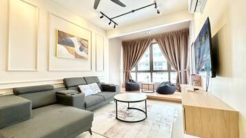 A modern living room with a grey sofa, a round coffee table, and a flat-screen TV mounted on the wall.
