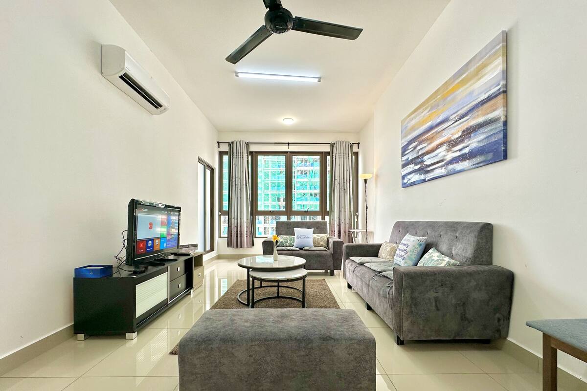 Un salon moderne avec un canapé gris, un pouf gris, un téléviseur posé sur un meuble et un tableau accroché au mur.
