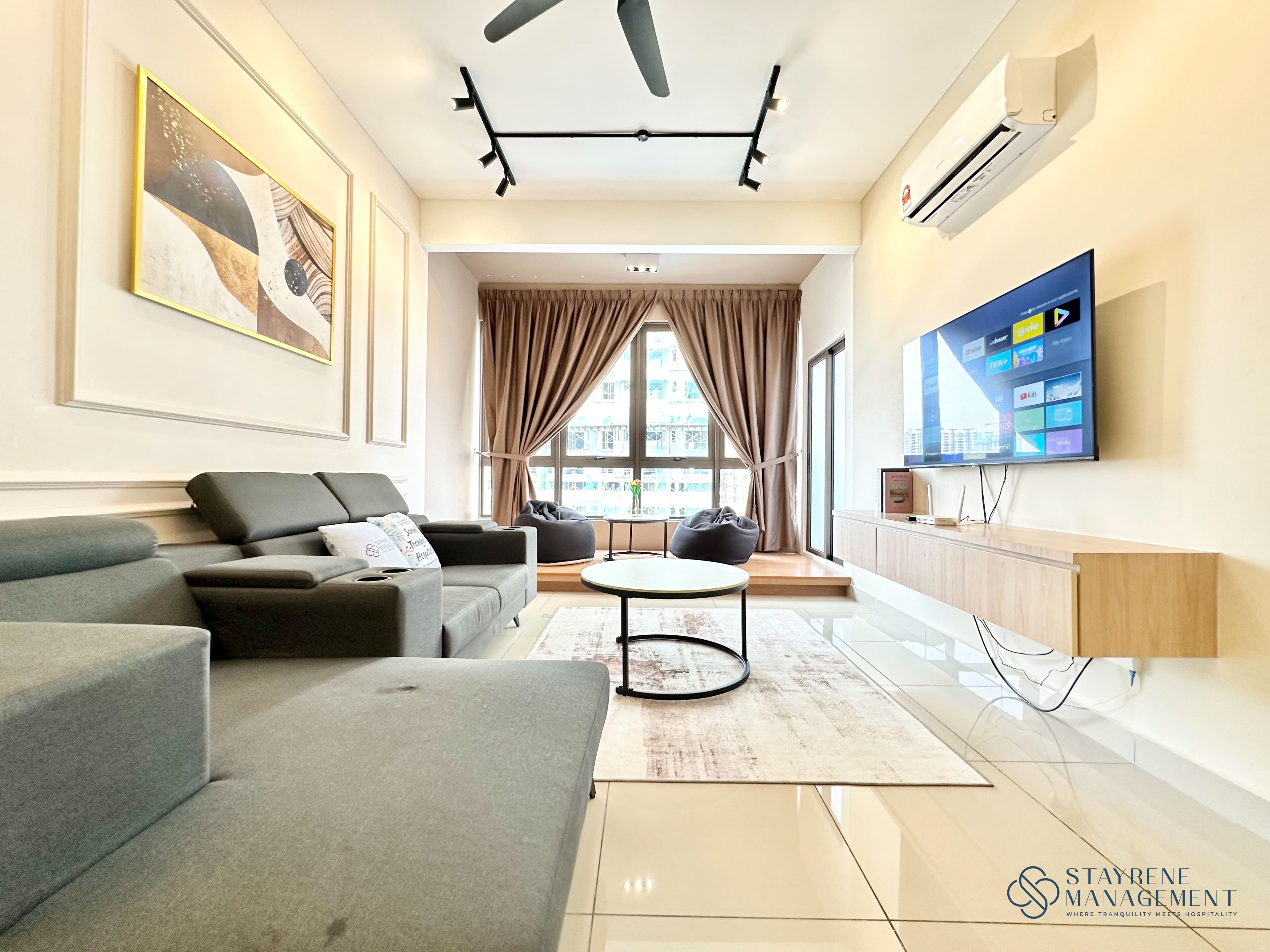 A modern living room with a grey sofa, a round coffee table, and a TV mounted on the wall.