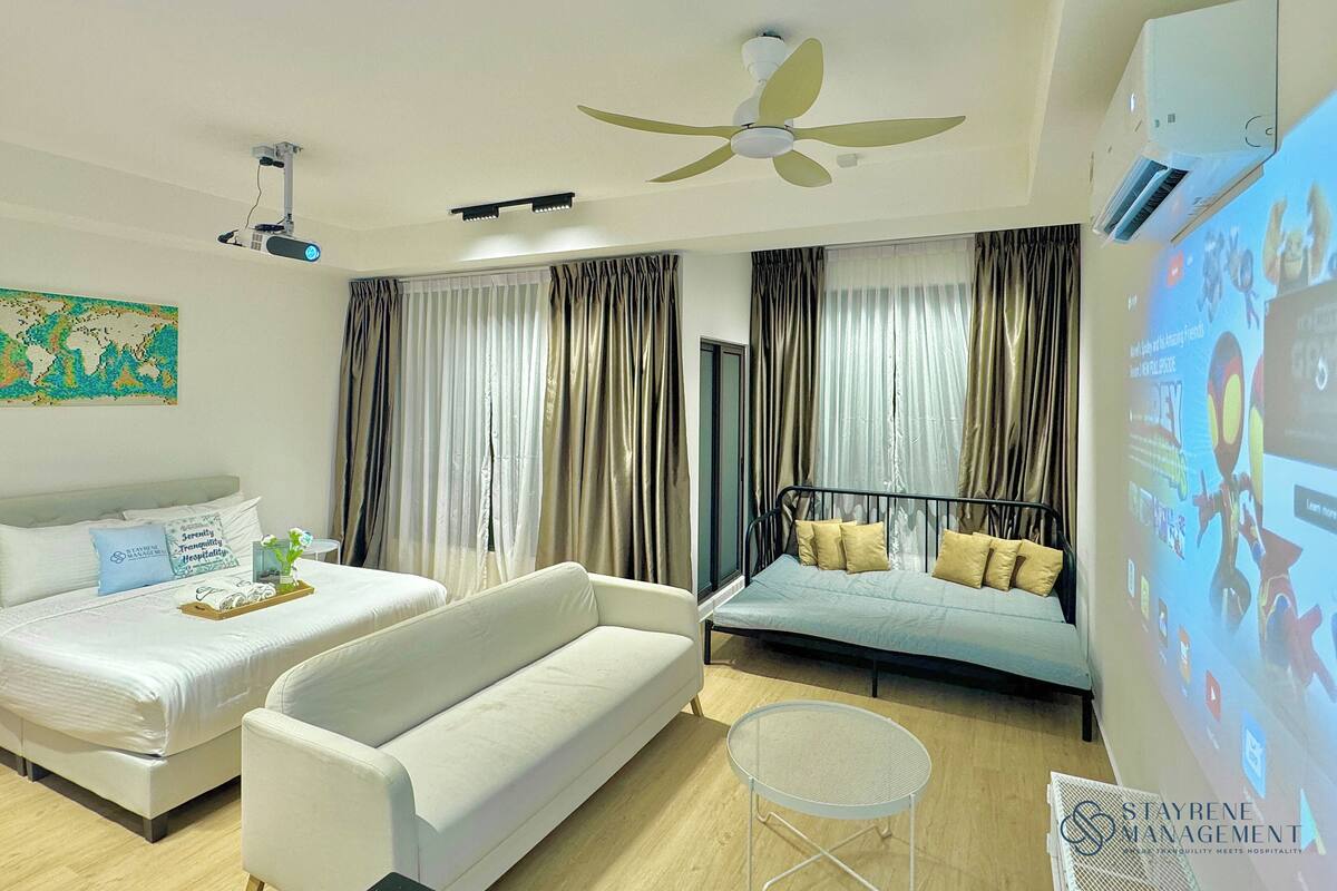 Une chambre d’hôtel moderne équipée d’un canapé-lit, d’un lit séparé, d’un ventilateur de plafond, d’un écran de projection et d’une œuvre d’art représentant une carte du monde.