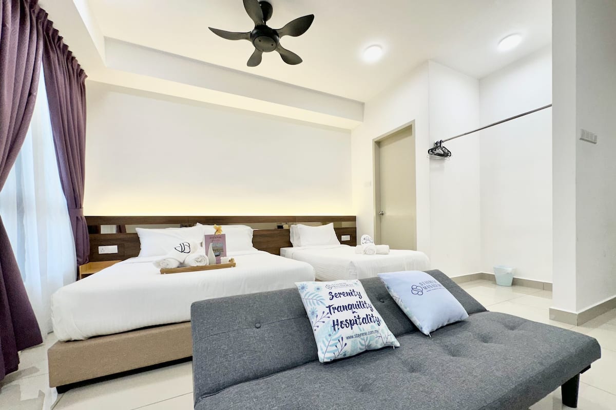 Une chambre d’hôtel moderne avec deux lits, un canapé gris et un ventilateur de plafond.