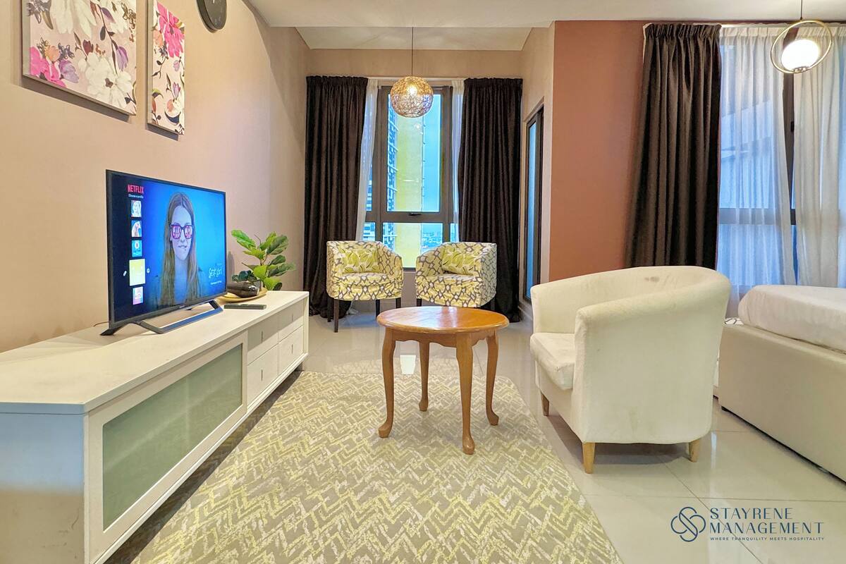 Un salon moderne avec un téléviseur à écran plat, deux fauteuils à motifs, un canapé blanc et une plante décorative.