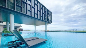 Una piscina moderna de hotel con agua cristalina, una zona cubierta con sillones de descanso y vistas al mar.