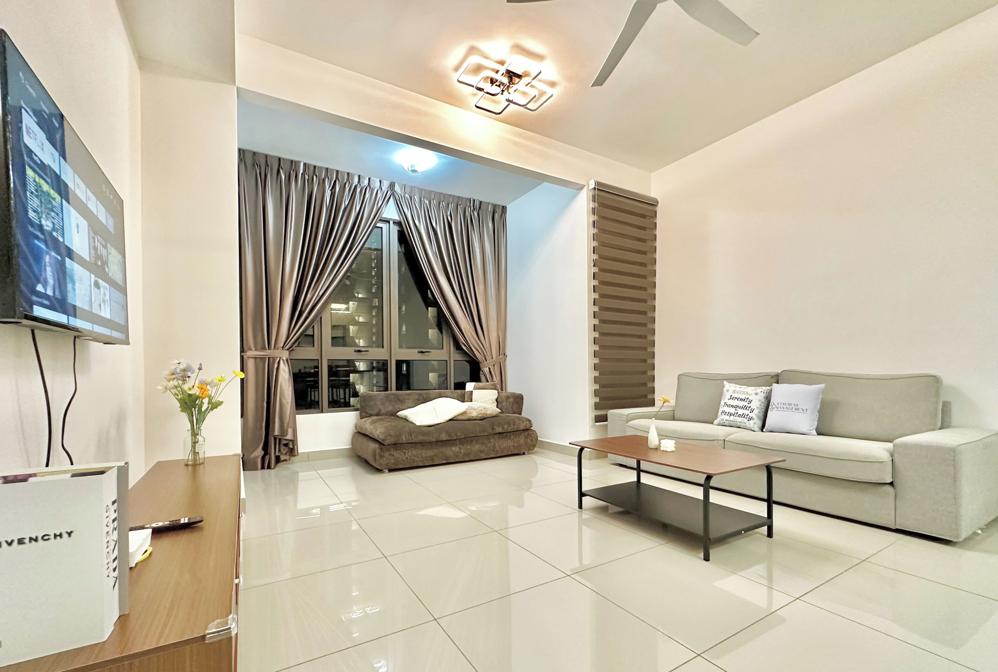 A modern living room with a sofa, a coffee table, a TV, and a large window with curtains.
