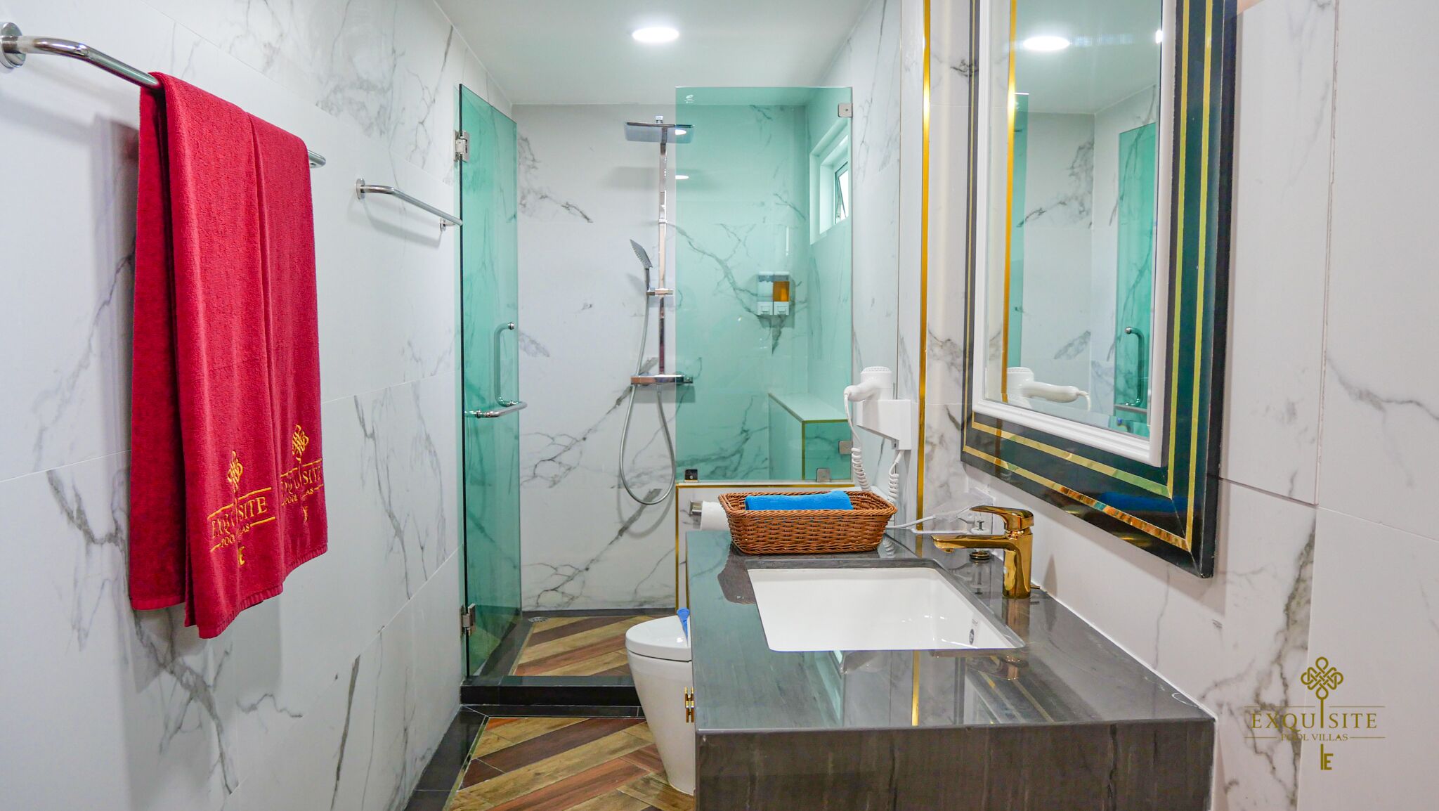 Une salle de bain avec un mur en marbre, une serviette rouge, une cabine de douche en verre, un lavabo avec un robinet doré et un miroir avec un cadre doré.