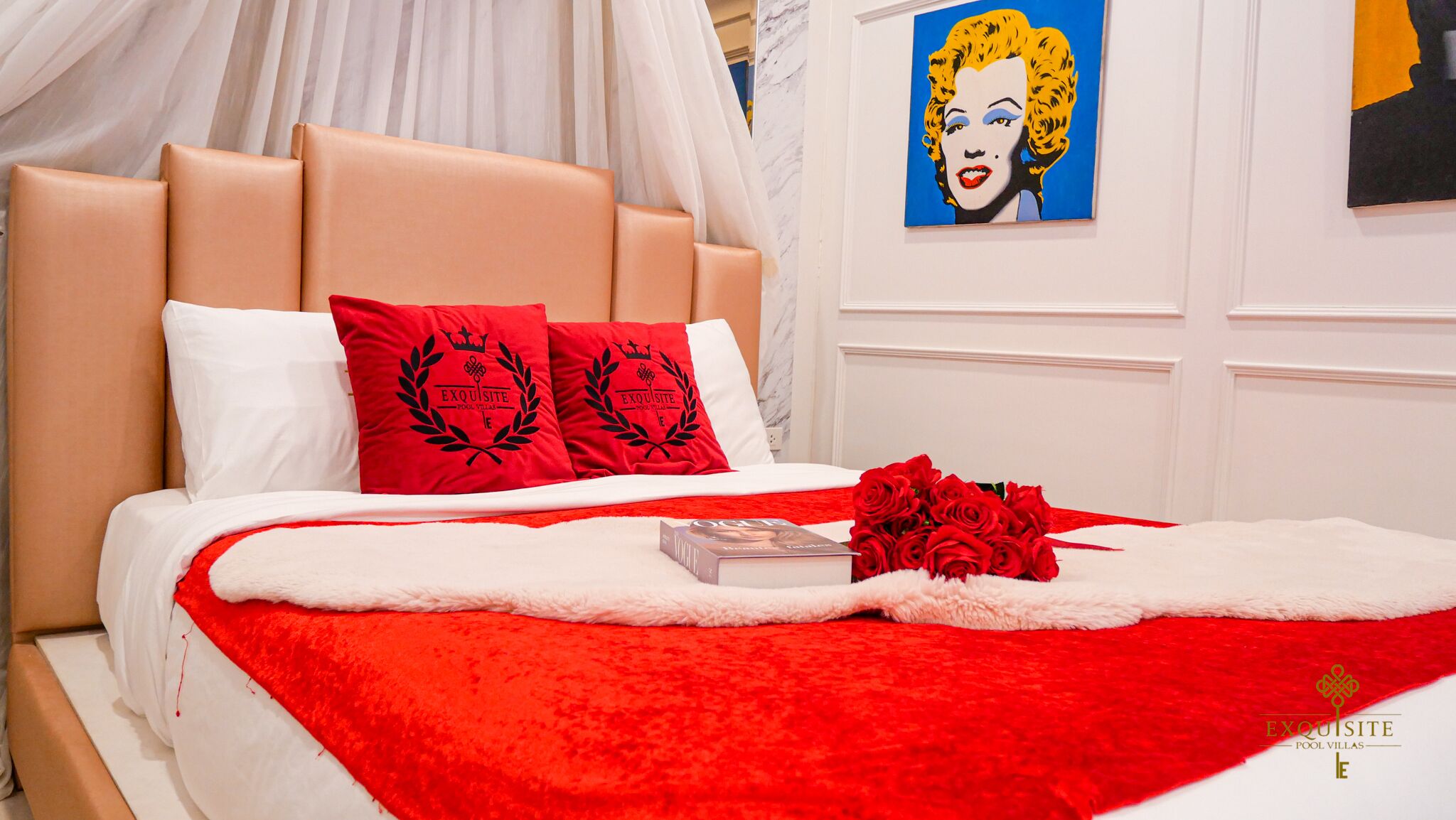 Un letto con una coperta rossa, due cuscini rossi, un bouquet di rose rosse e un libro intitolato 