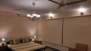 Quarto com cama, mesas de cabeceira, uma cadeira, ventoinha no teto e luminária na parede.