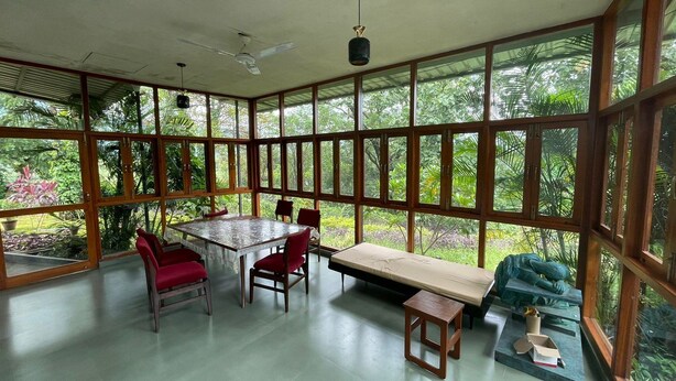 Um quarto amplo com grandes janelas, uma mesa, cadeiras e um banco.