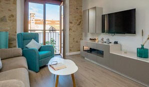 A modern living room with a teal armchair, a white coffee table, and a flat-screen TV mounted on the wall.