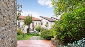 A courtyard with a paved walkway, stone wall, and a building with a red roof. - Holiday Apartment "Nigella Langhe Home" with Mountain View, Balcony & Wi-Fi (Niella Belbo)