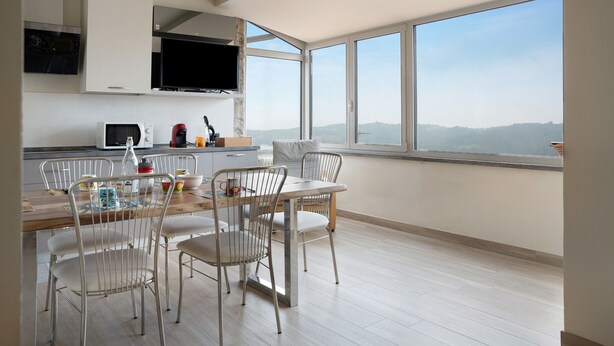 A modern kitchen with white cabinetry, a flat-screen TV, and a dining area with metal chairs and a wooden table. - Holiday Apartment "Nigella Langhe Home" with Mountain View, Balcony & Wi-Fi (Niella Belbo)