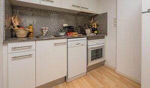 Cozinha moderna com armários brancos, bancadas de granito, lava-louças e forno.