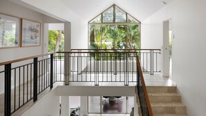 Et moderne interiør med en trappe, en balkon med glasgelændere og udsigt til grøn vegetation udenfor.