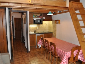 A compact kitchen with a dining area, wooden cabinets, a microwave, and a tiled backsplash.