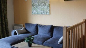 A living room with a sofa, a coffee table, a potted plant, a painting, and a wall-mounted light fixture. - Duplex T3 in Jausiers - 6 people, terrace, parking (Jausiers)