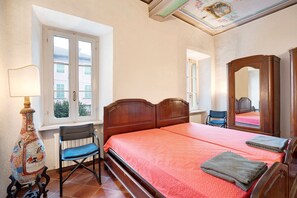 Une chambre à coucher avec un lit, une chaise, une lampe, une fenêtre et un miroir.