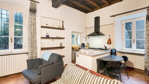 A cozy living area with a sofa, a dining table with chairs, a kitchen area with a stove, and a window with curtains. - Apartment 'In Villa Belli' with Shared Garden & Wi-Fi (Miasino)