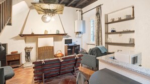 A rustic room with a wooden bench, a television, a fireplace, and shelves with kitchenware. - Apartment 'In Villa Belli' with Shared Garden & Wi-Fi (Miasino)