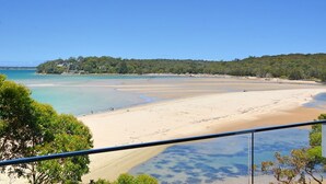 Une plage aux eaux d’un bleu limpide, bordée de sable fin, avec une colline boisée en arrière-plan.
