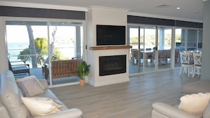Un vaste salon doté d’une cheminée, d’un téléviseur fixé au-dessus et d’un balcon offrant une vue sur la mer.