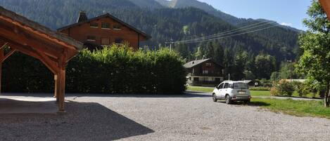 A building with a wooden structure in the foreground, a gravel driveway, and a white car parked in the distance.