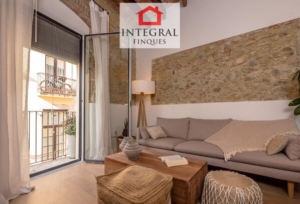 A living room with a stone wall, a sofa, a coffee table, and a balcony with a bicycle. - Modern duplex in Palamós center with terrace and private garage (Palamós)