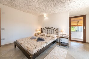 A bedroom with a bed, bedside lamps, a small table, and a view through a glass door.