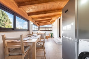 A modern kitchen with wooden ceiling beams, a stainless steel refrigerator, and a dining area with wooden tables and chairs.