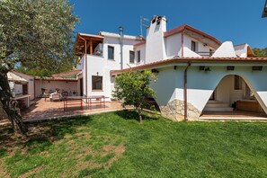 A modern house with a patio, a stone wall, and a staircase leading to an upper level.
