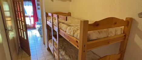 Una habitación con literas, un estante de madera y suelo de baldosas.