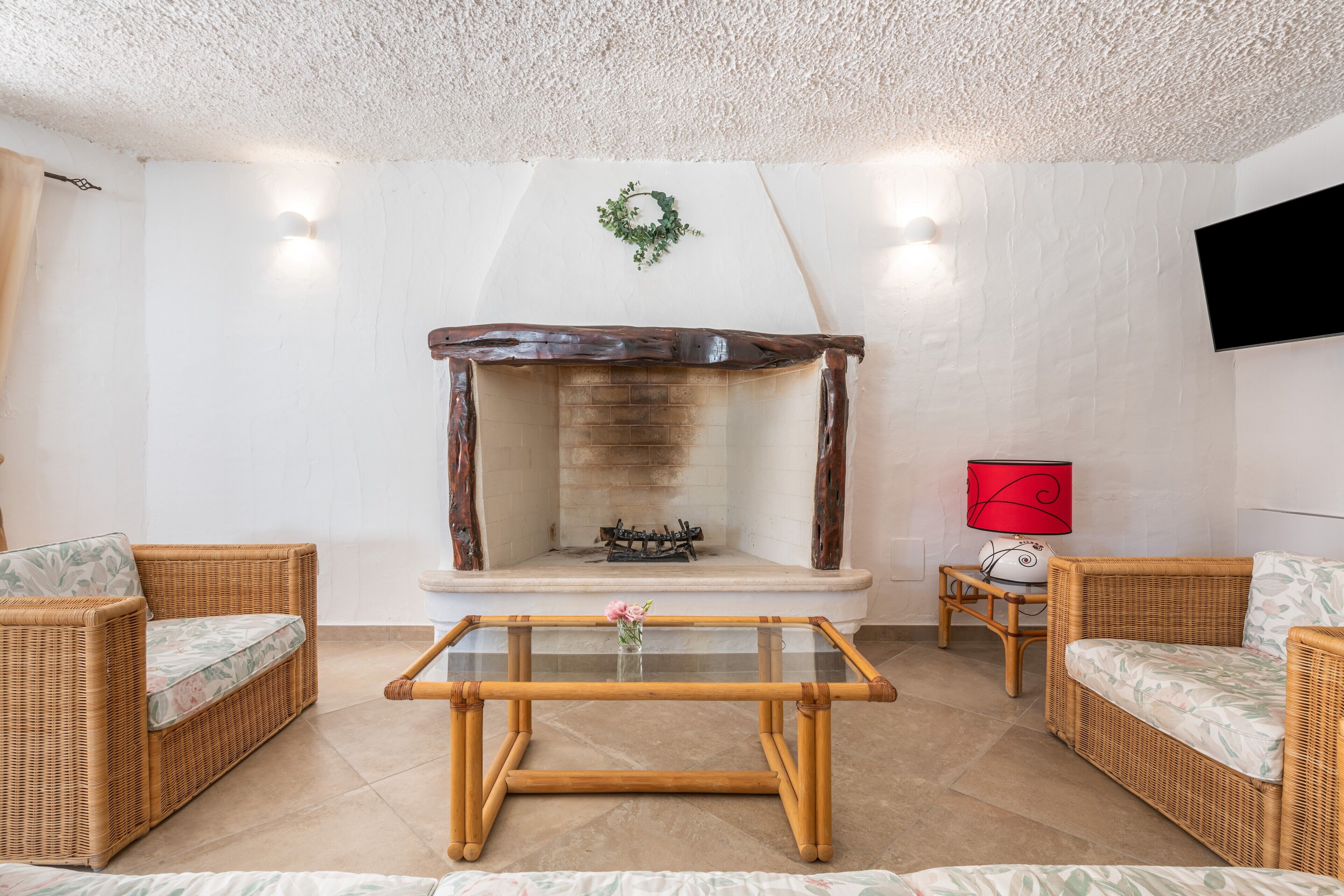 A living room with wicker furniture, a glass-top coffee table, a fireplace, and a flat-screen TV mounted on the wall.
