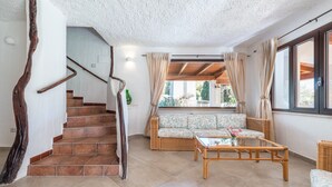 Un vaste espace de vie comprenant un escalier, des meubles en osier et une grande fenêtre.