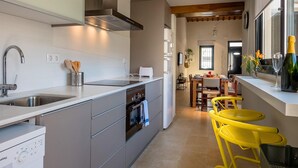 Una cocina moderna con horno empotrado, lavavajillas y pileta. Hay un comedor con sillas amarillas y una mesa.