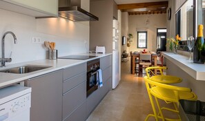 A modern kitchen with a built-in oven, a dishwasher, and a sink. There is a dining area with yellow chairs and a table. - Beachfront Fisherman's Cottage with AC, Wi-Fi & Parking (Palamós)